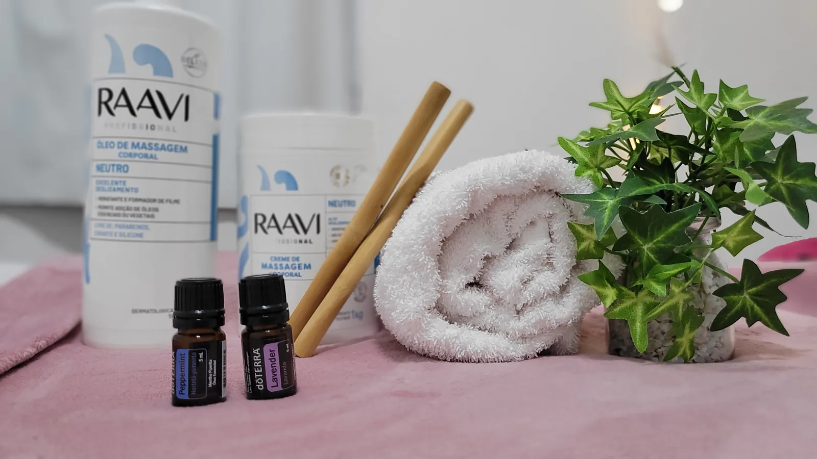 Bancada de massagem com óleo e creme corporal, óleos essenciais de hortelã-pimenta e lavanda, bambus e toalha enrolada sobre a maca