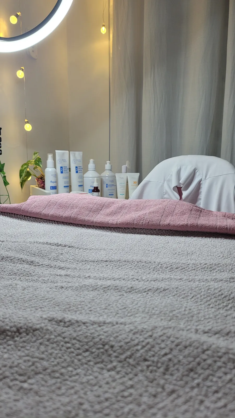 Sala de atendimento com a maca forrada, o ring light e os produtos de cuidado da pele na bancada